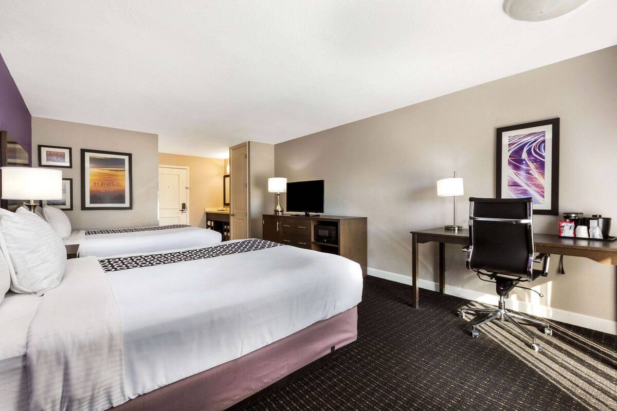 Une chambre d’hôtel avec deux lits, un bureau, une chaise, une télévision et une lampe de bureau.