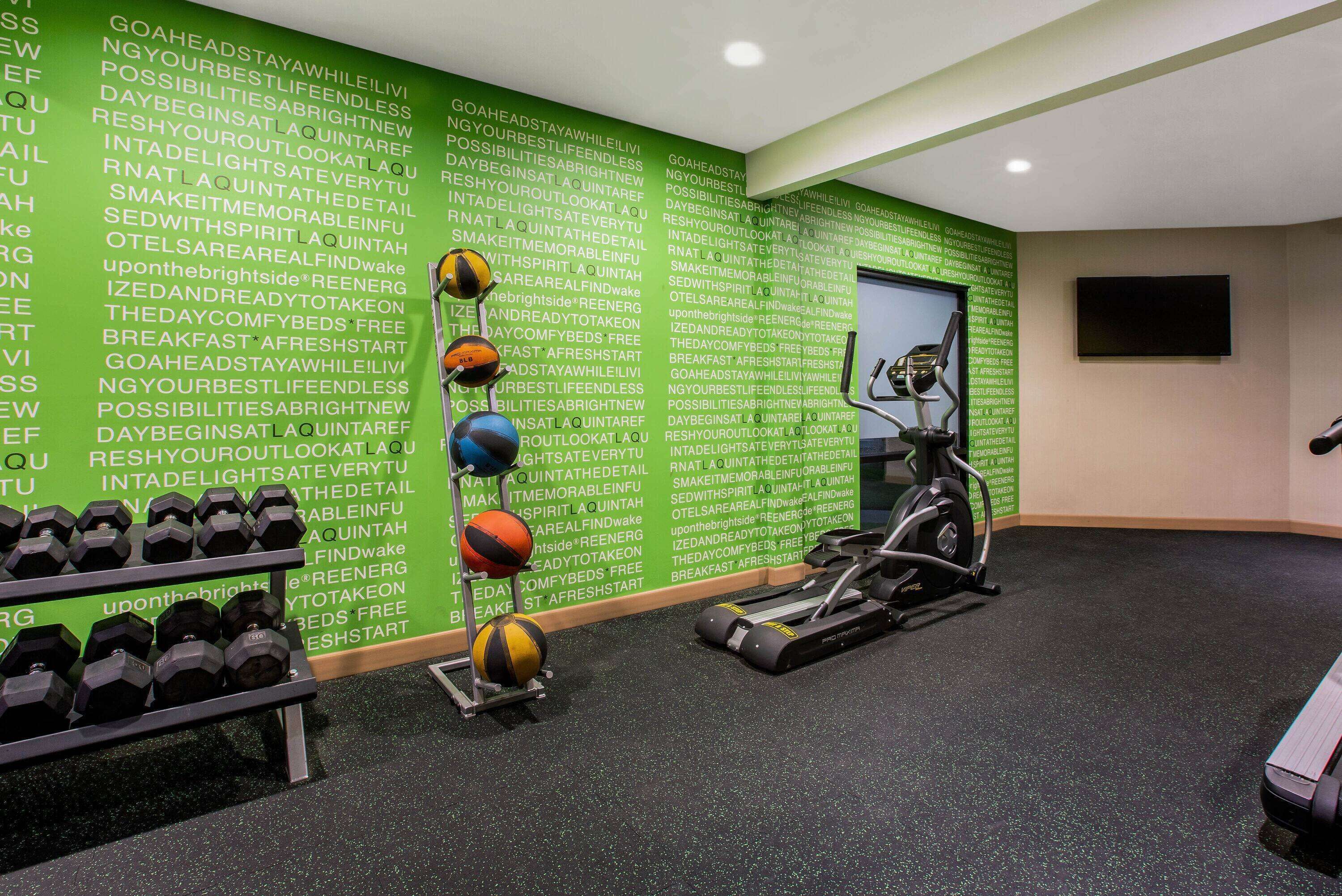 A gym with exercise equipment, a wall with motivational text, and a television screen.