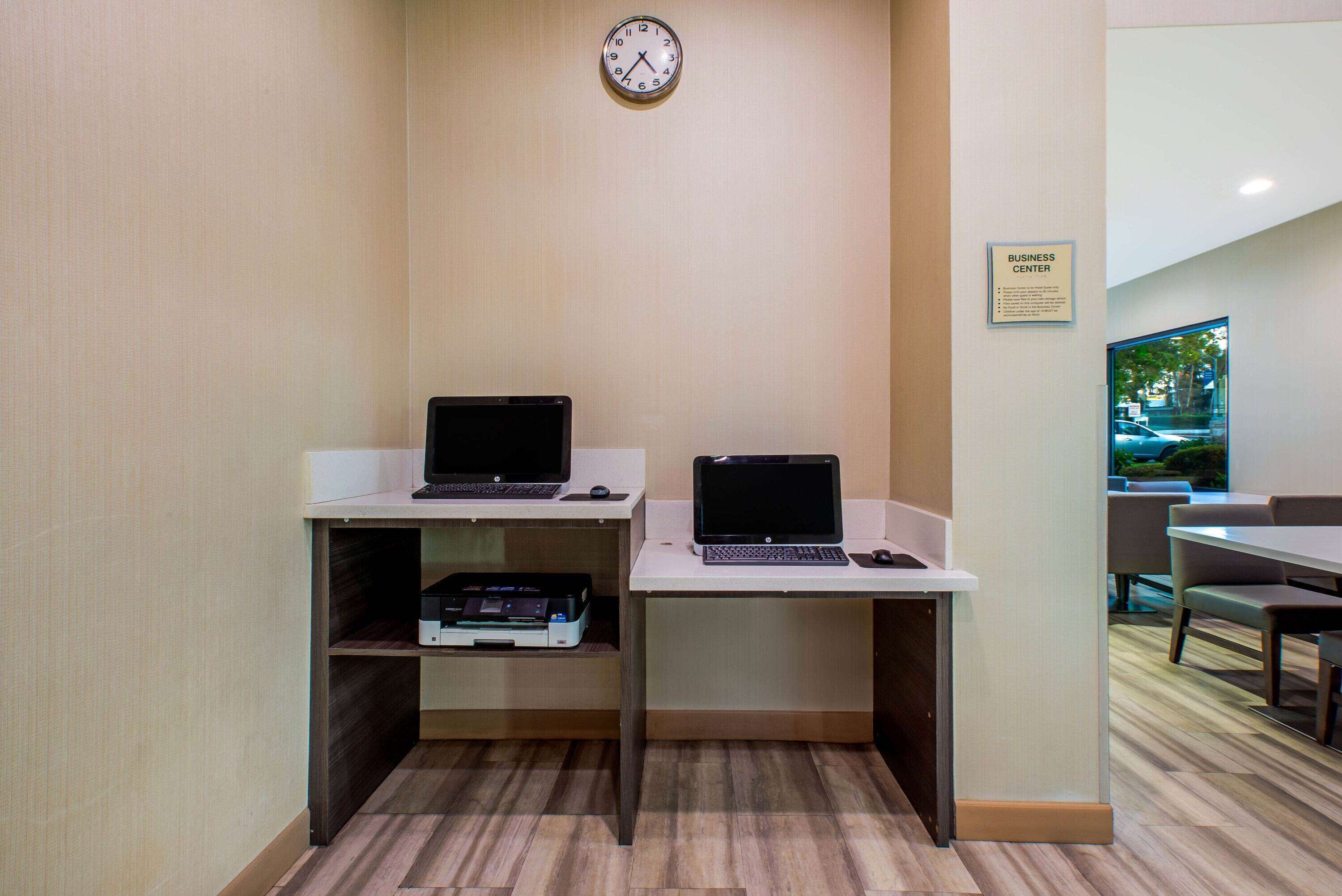 A business center with two desks, each with a laptop and a mouse, and a clock on the wall.