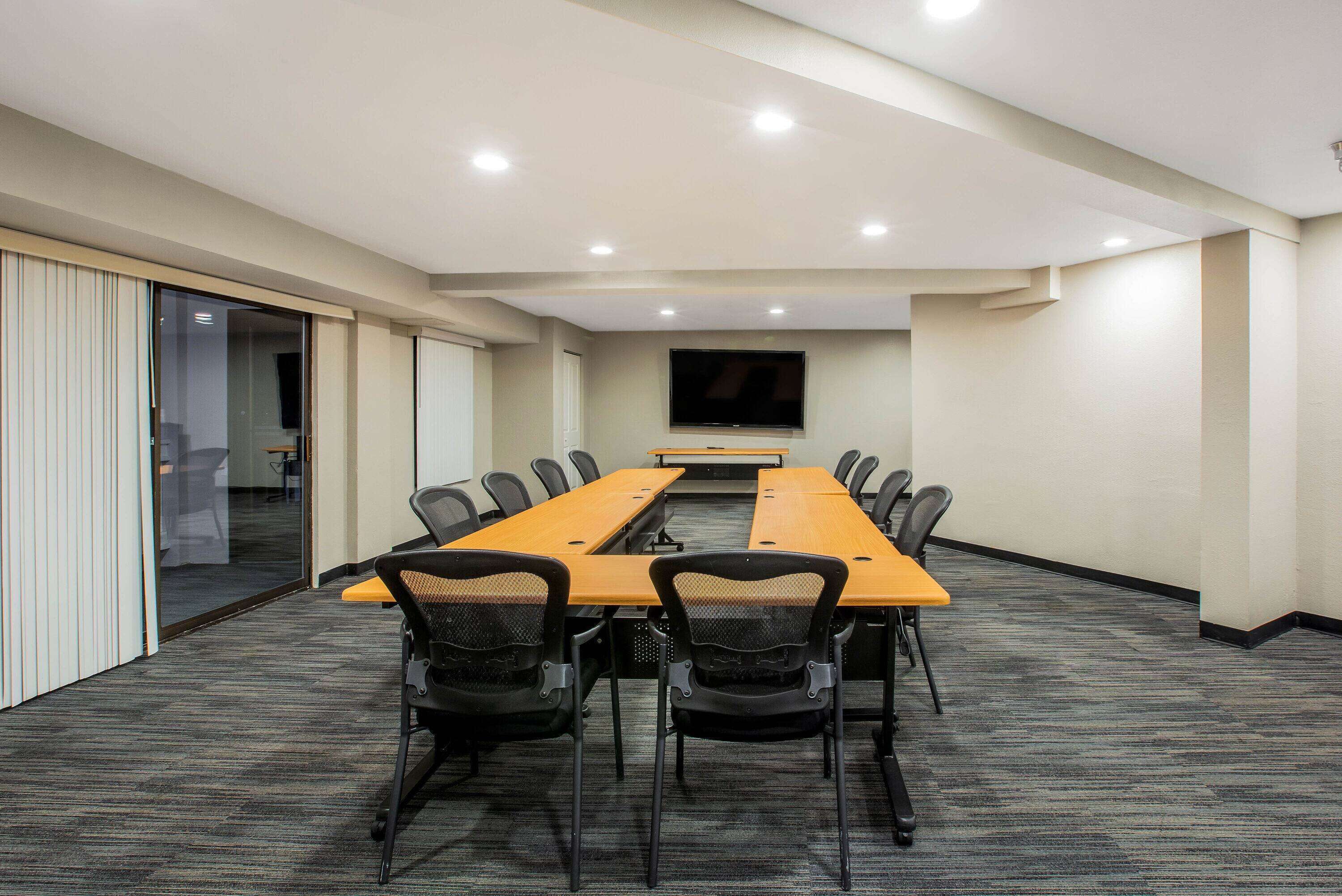 A conference room with a long table, chairs, a flat-screen TV, and a carpeted floor.
