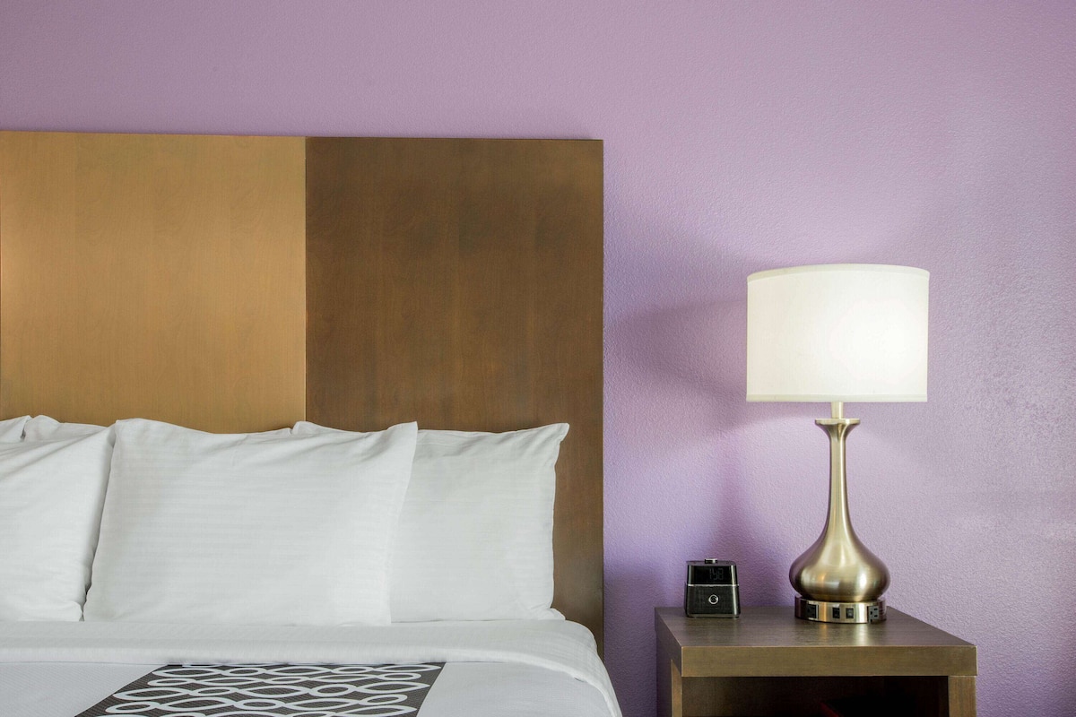 Une chambre d’hôtel comprenant un lit, une table de chevet, une lampe et un mur orné d’un panneau en bois.