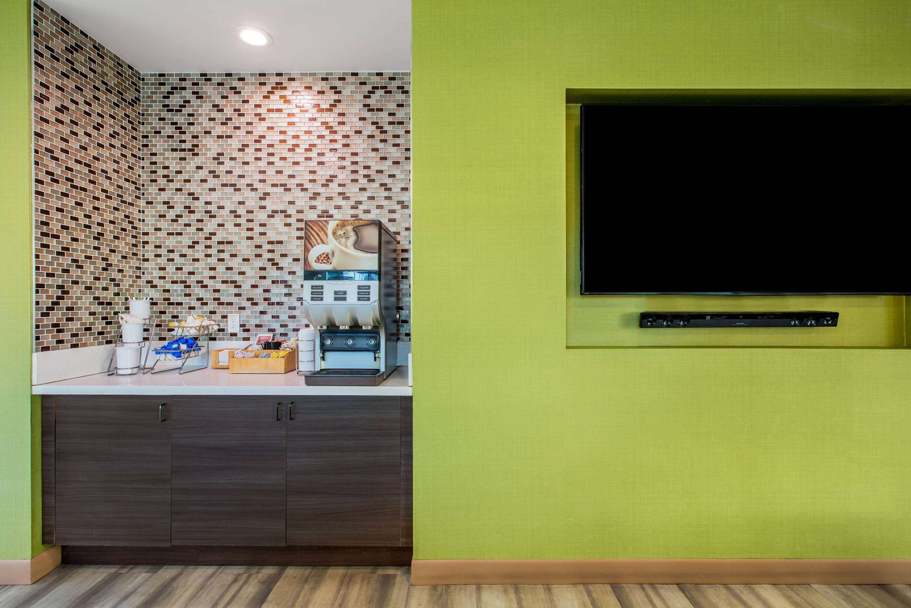 Una kitchenette con salpicadero de azulejos, una cafetera y un televisor de pantalla plana montado en la pared.