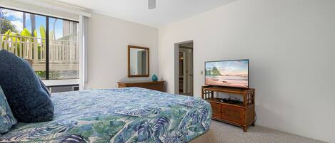 A bedroom with a bed, a ceiling fan, a television, and a view of the outdoors through a sliding door.