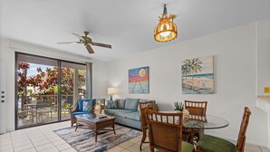 A spacious living room with a glass dining table, comfortable seating, a ceiling fan, and artwork on the walls. - Wailea Grand Champions - Maui Condo & Home (Kihei)