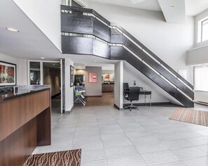 A modern hotel lobby with a central reception desk, a staircase, and a seating area.