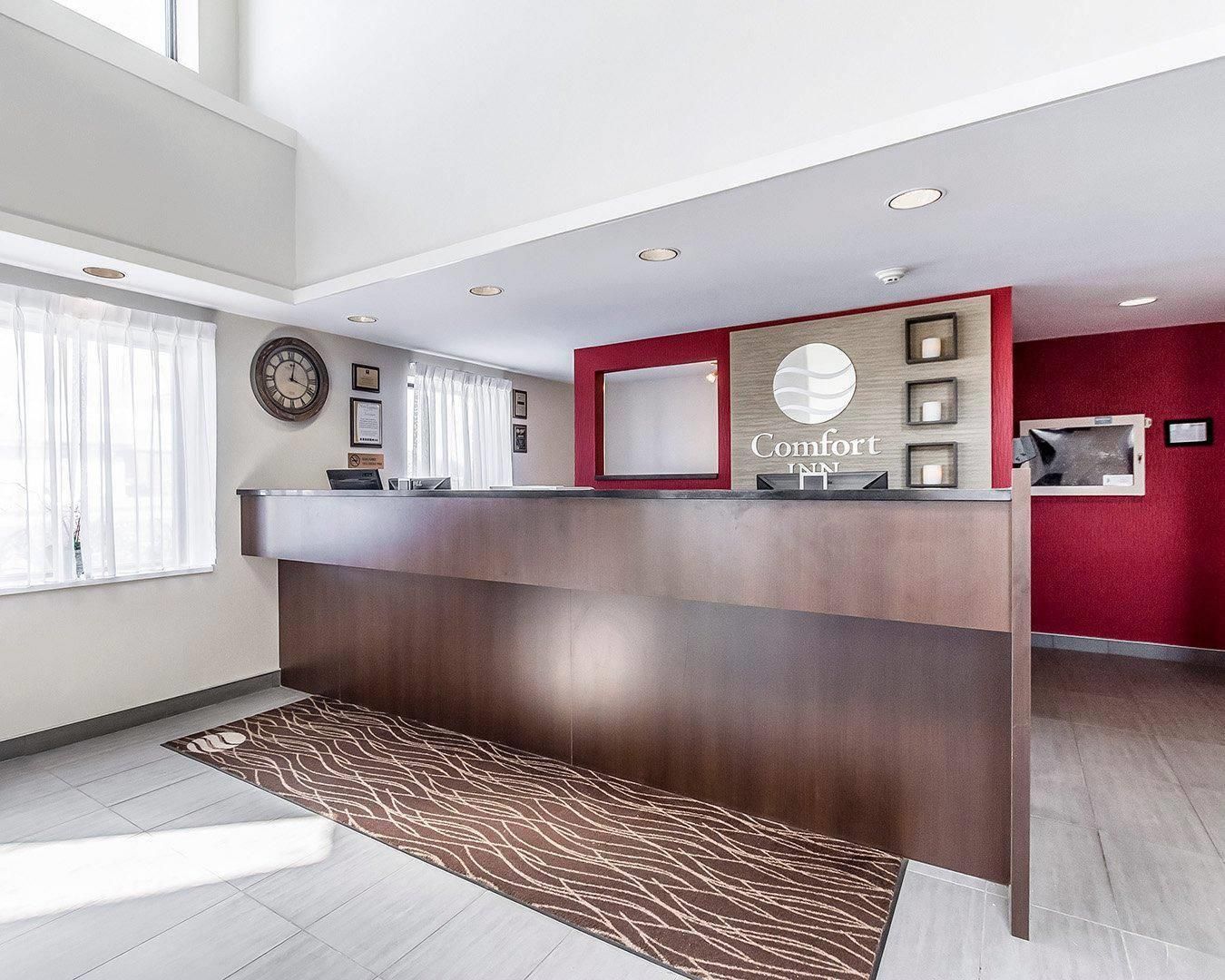 A hotel reception area with a reception desk, a clock, and a red accent wall.