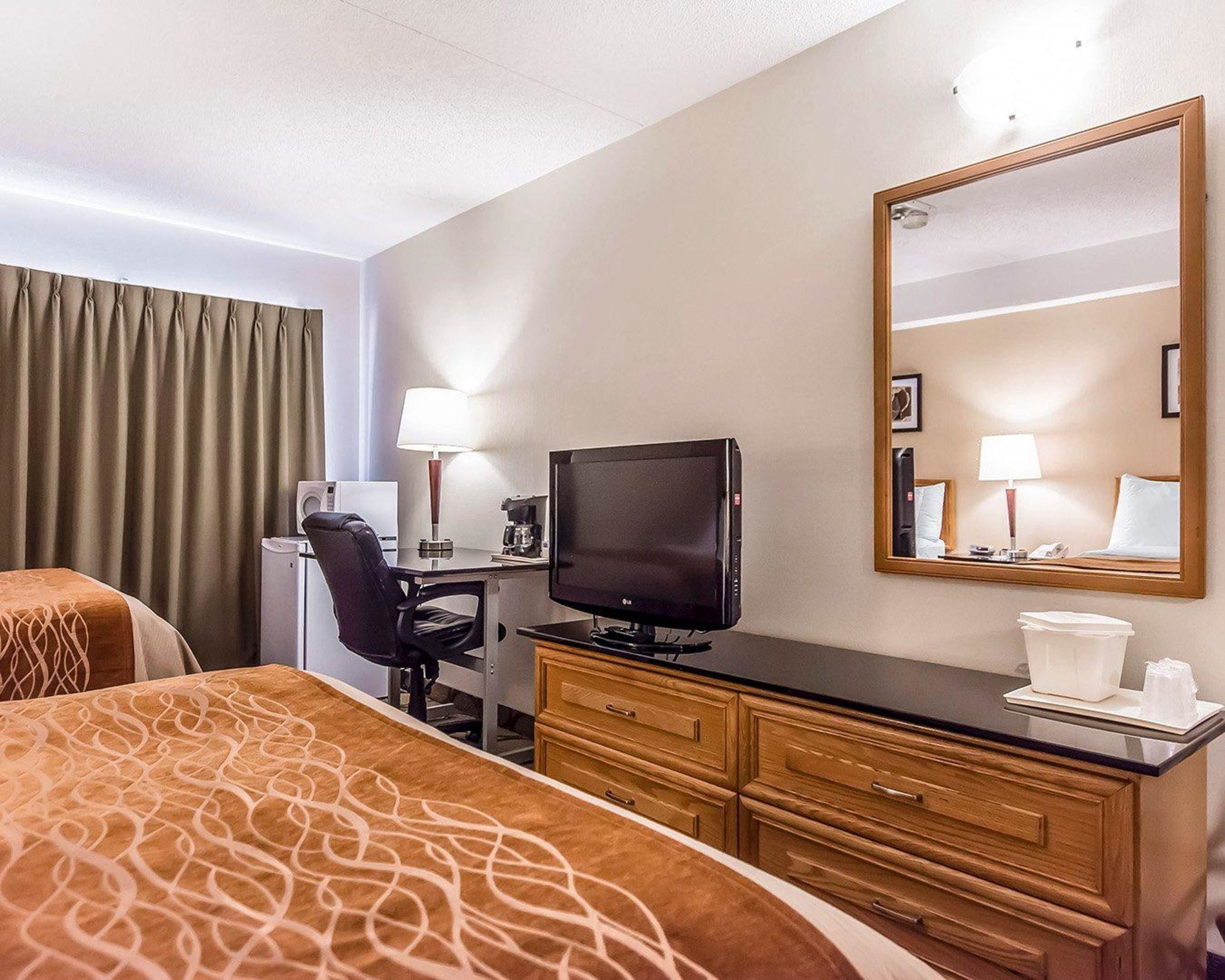 A hotel room with two beds, a desk with a television, a mirror, and a dresser.