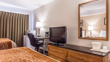 A hotel room with two beds, a desk with a television, a mirror, and a dresser.