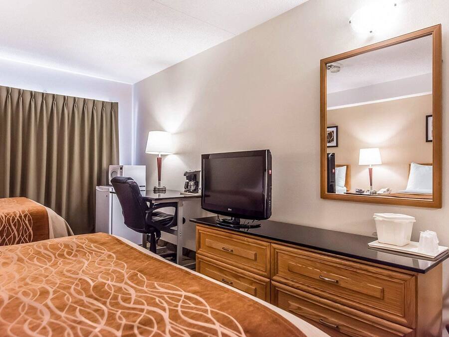 A hotel room with two beds, a desk with a television, a mirror, and a dresser.