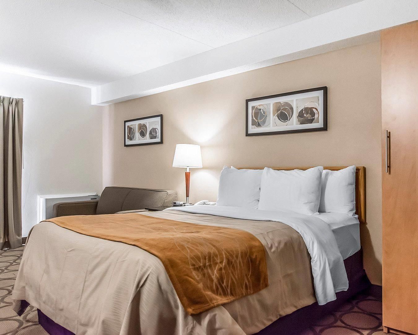 A hotel room with a bed, a desk, a lamp, and two framed pictures on the wall.