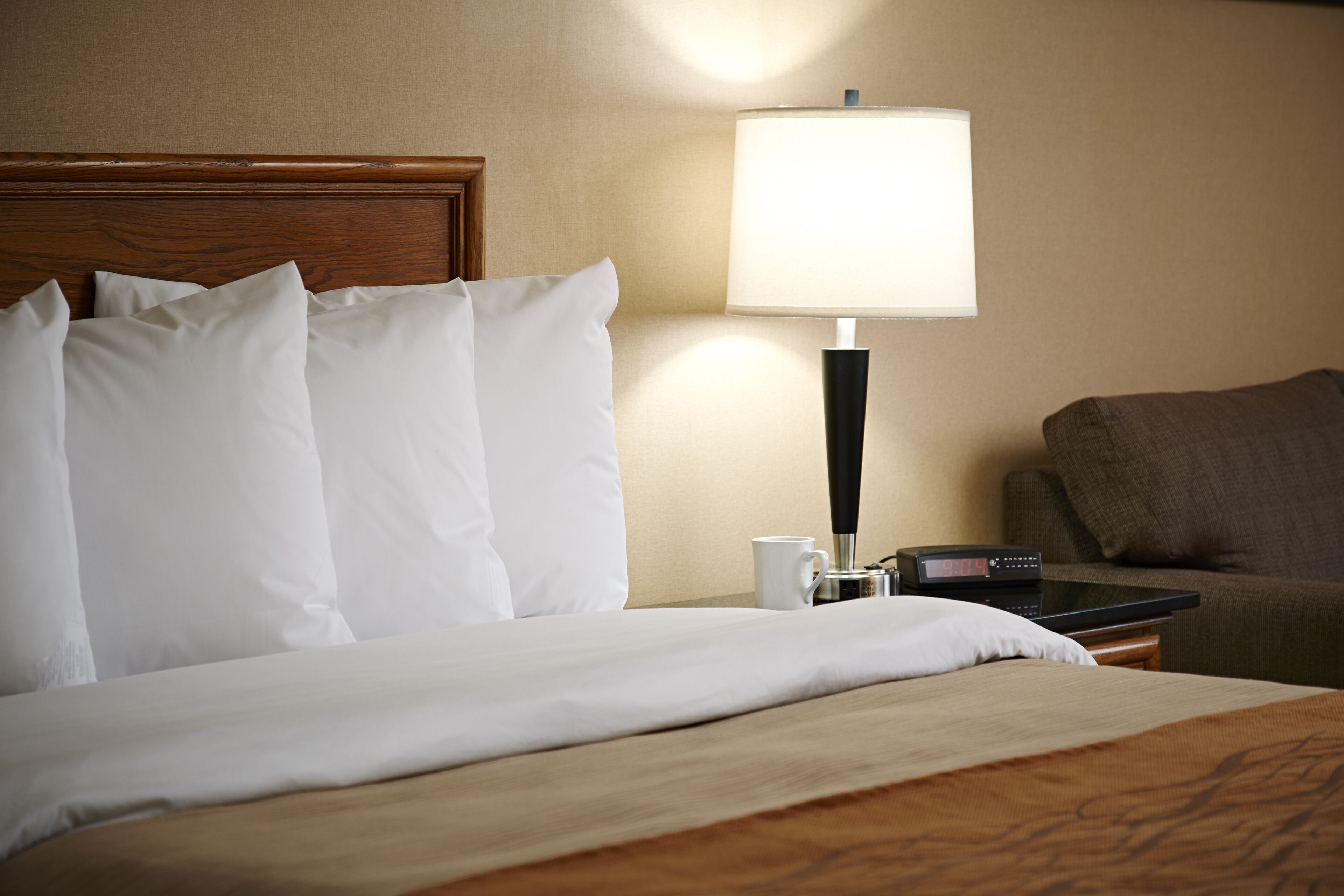 A hotel room with a neatly made bed, a bedside lamp, a remote control, and a brown sofa.