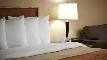 A hotel room with a neatly made bed, a bedside lamp, a remote control, and a brown sofa.