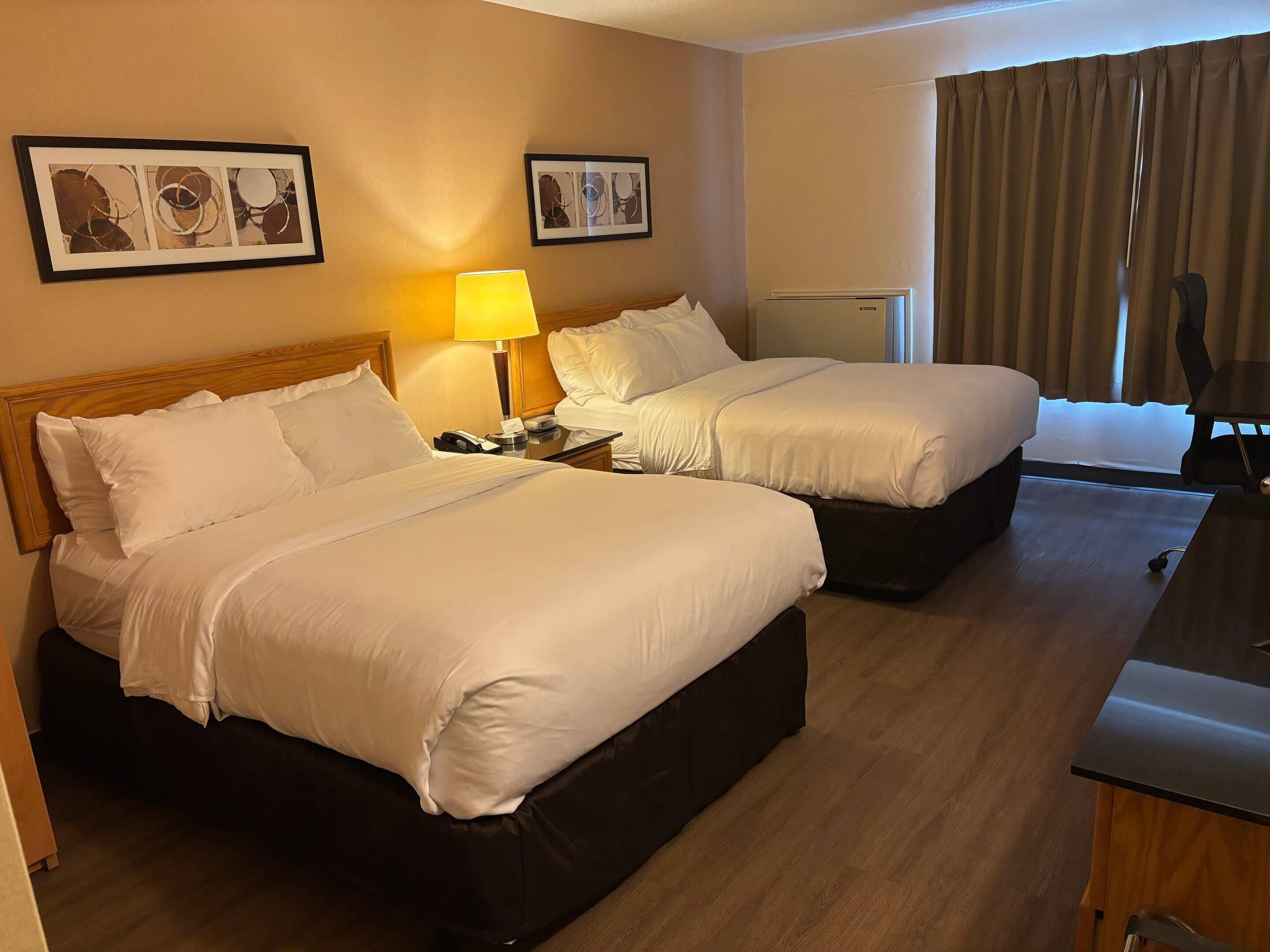 Une chambre d’hôtel avec deux lits, un bureau, une lampe et des œuvres d’art accrochées aux murs.