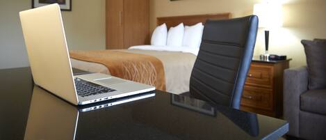 Een hotelkamer met een bed, een bureau met een laptop, een stoel, een nachtkastje en een lamp.