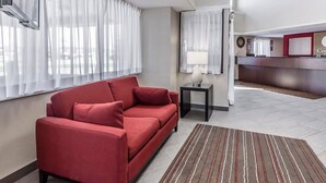 Eine Hotelhalle mit einer roten Couch, einem kleinen Tisch mit Lampe, einem Empfangsbereich und einem Streifenmuster-Teppich.