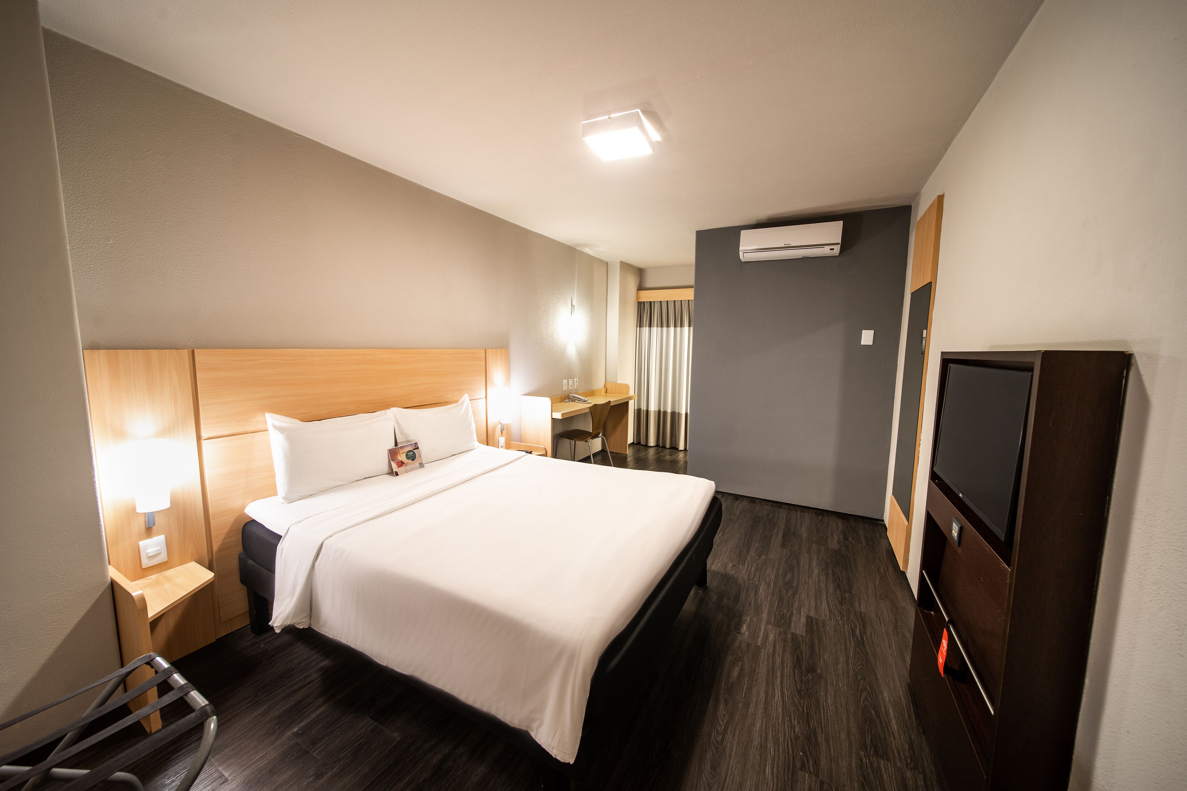 A hotel room with a large bed, bedside lamps, a desk, and a television.