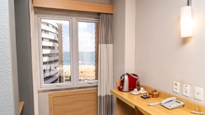 Habitación de hotel con escritorio de madera, cafetera, teléfono y vistas a un edificio y la playa.