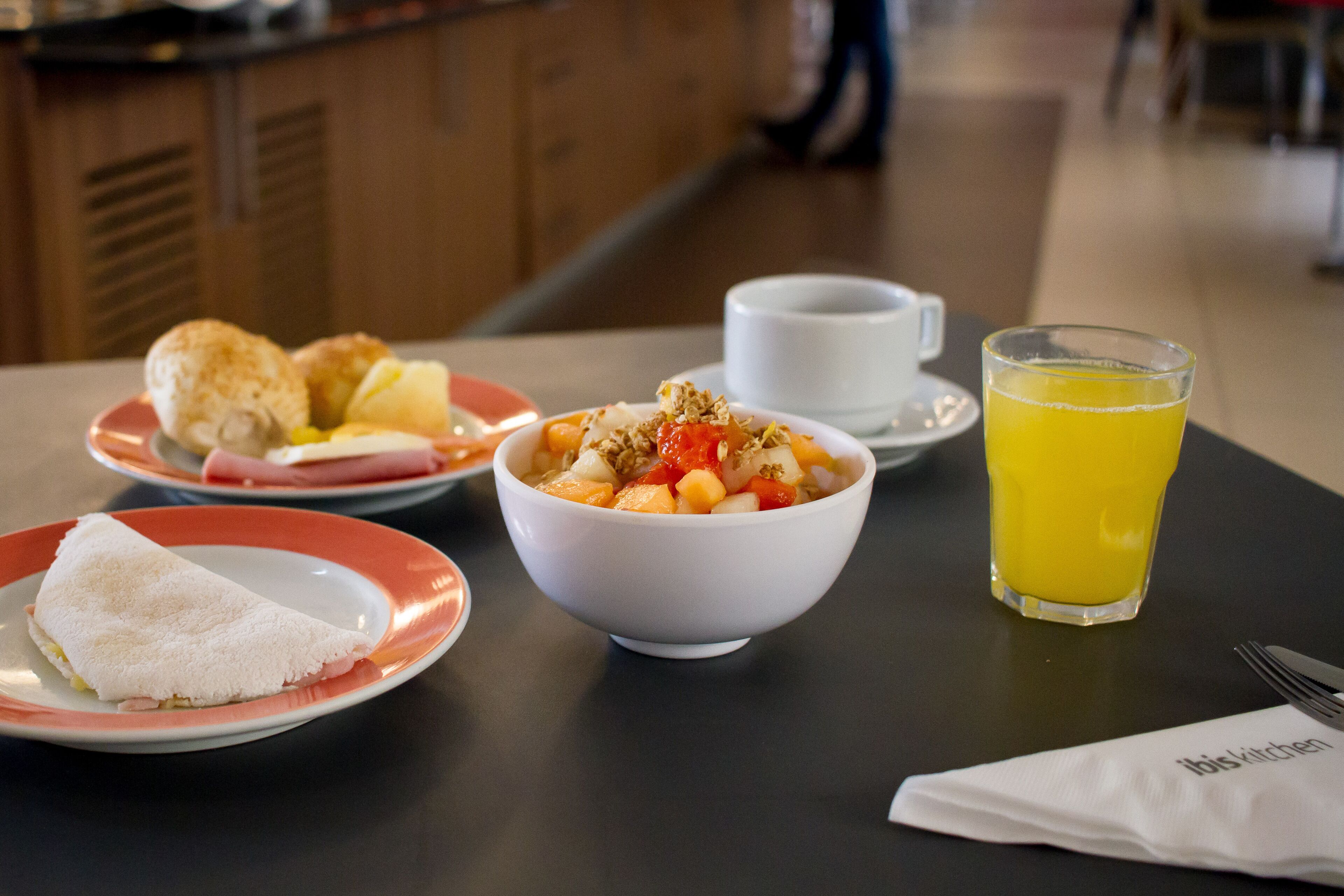 Un desayuno con ensalada de frutas, un croissant, un vaso de zumo de naranja y una taza sobre una mesa.