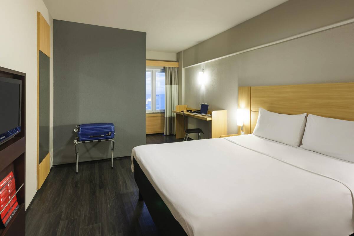 Una habitación de hotel con cama, escritorio, silla, televisor y maleta.