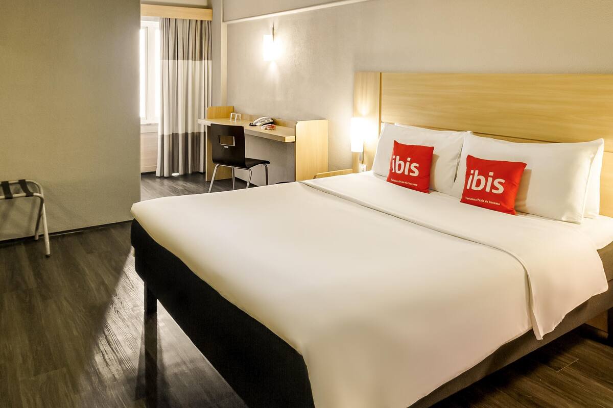 Habitación de hotel con cama, escritorio, silla y lámpara.
