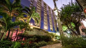 Un hotel de varios pisos con fachada azul, rodeado de abundante vegetación y un camino pavimentado.