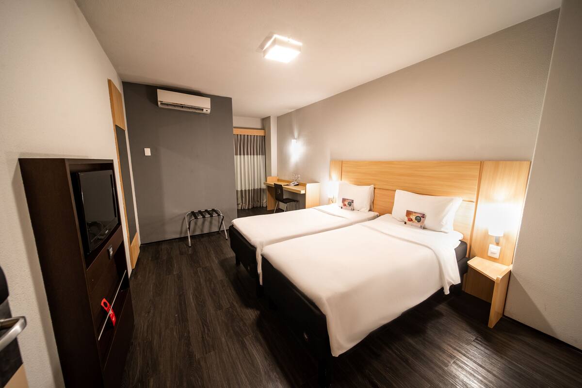 Habitación de hotel con dos camas, un escritorio, una silla, un televisor y un equipo de aire acondicionado.