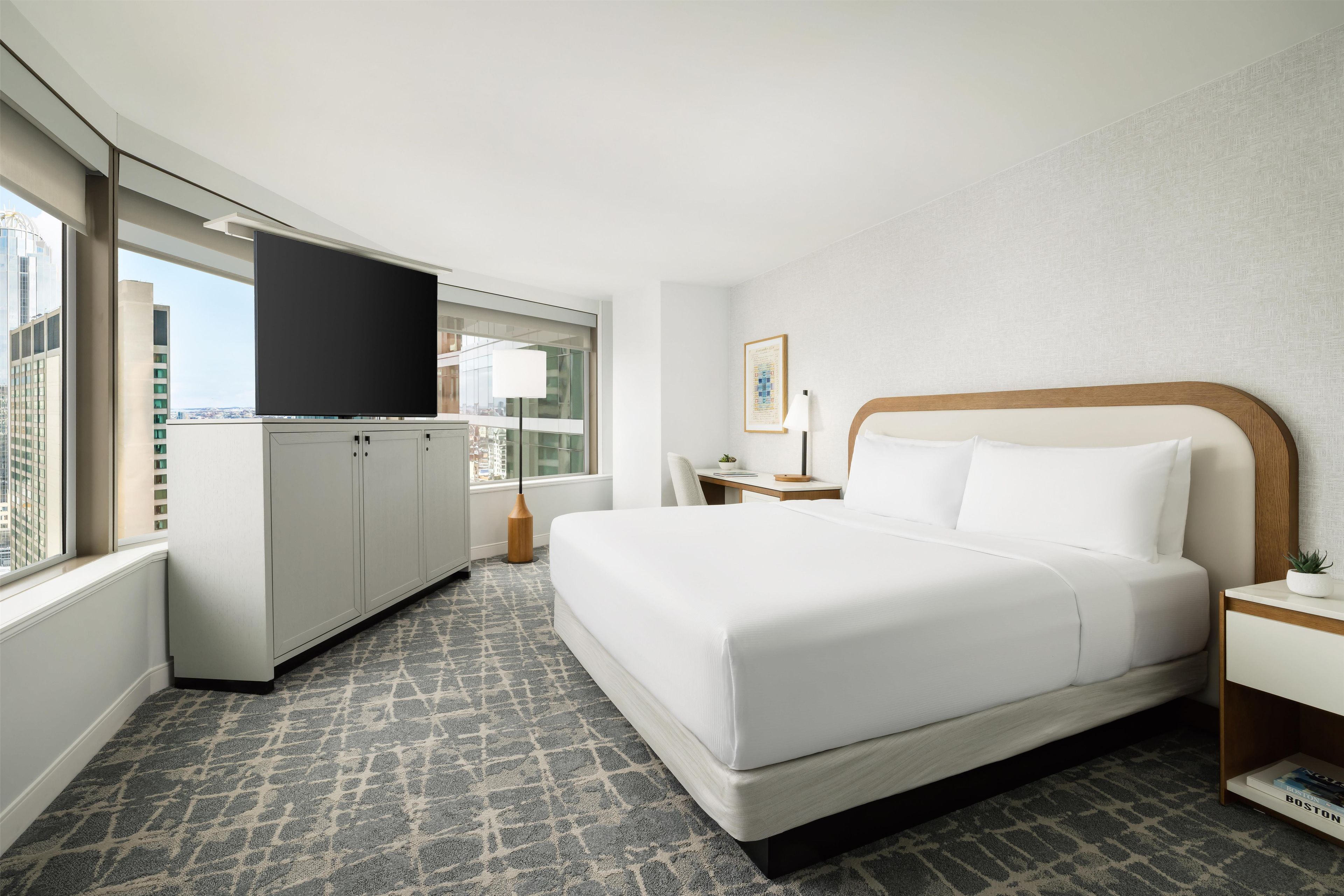 Habitación de hotel con cama, escritorio, televisor y ventana con vistas a la ciudad.