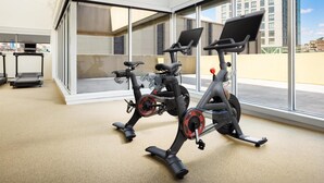 Un gimnasio con bicicletas estáticas, cinta de correr y amplias ventanas con vista a la ciudad.