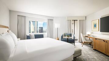 A hotel room with a large bed, a desk, a chair, and a view of the cityscape.