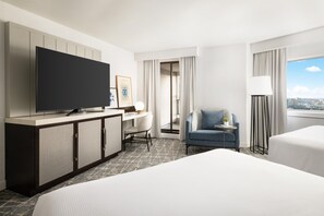 A hotel room with a bed, a desk with a chair, a television, a small table with a lamp, and a view of the city through the window. - Hilton Boston Back Bay (Boston)