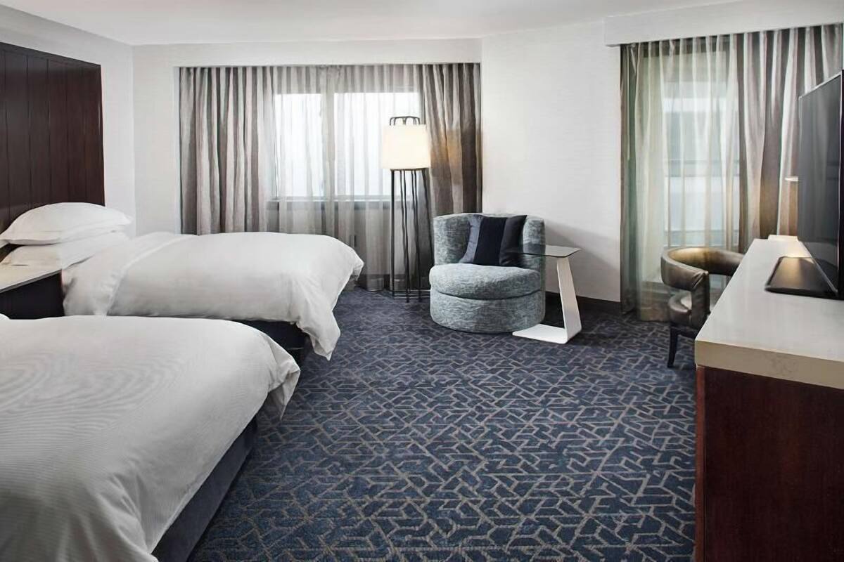 A hotel room with two beds, a desk, a chair, and a large window with curtains.