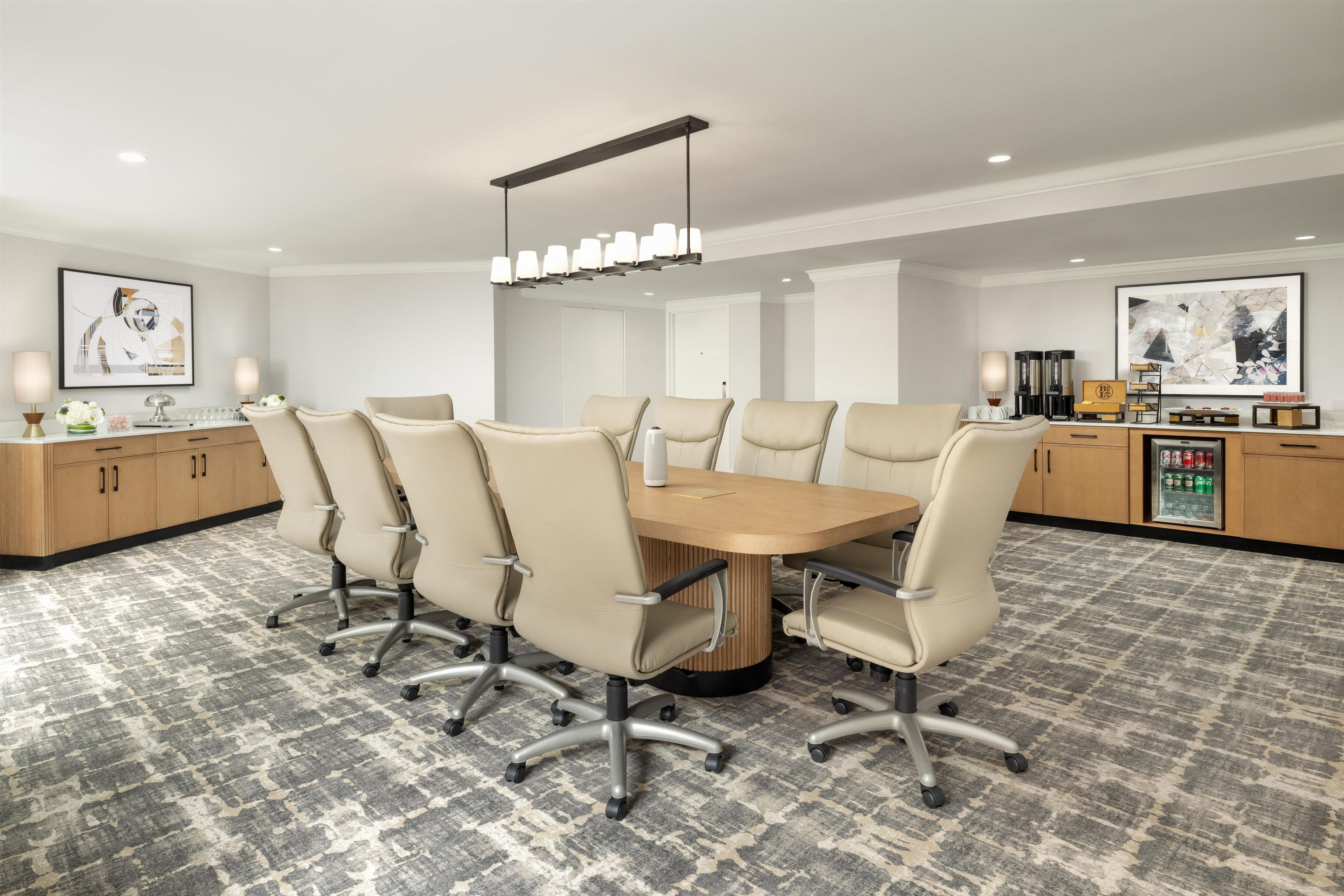 A conference room with a round table, six chairs, a modern chandelier, and artwork on the walls.