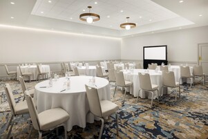 A conference room with round tables, chairs, a projector screen, and a carpeted floor.