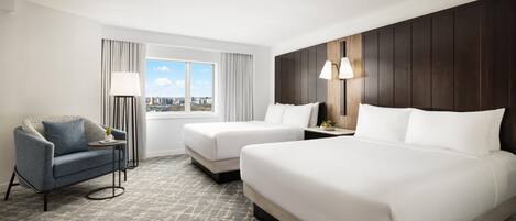 A hotel room with a large bed, two bedside tables, a chair, a window with curtains, and a view of the cityscape.