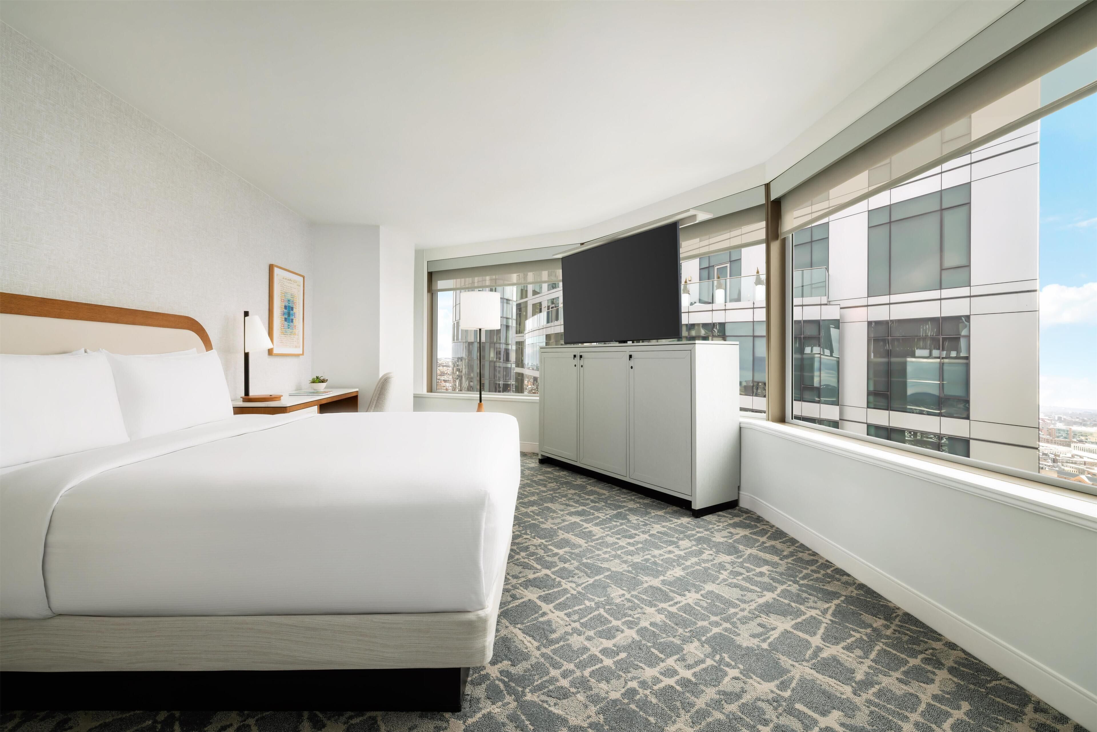 A hotel room with a large bed, a flat-screen TV, a desk, and a window with a city view.