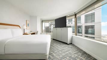 A hotel room with a large bed, a flat-screen TV, a desk, and a window with a city view.