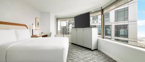 A hotel room with a large bed, a flat-screen TV, a desk, and a window with a city view.