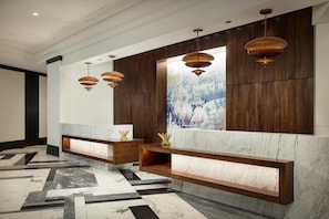 Un área de recepción con mostradores de mármol, estanterías de madera e iluminación colgante.