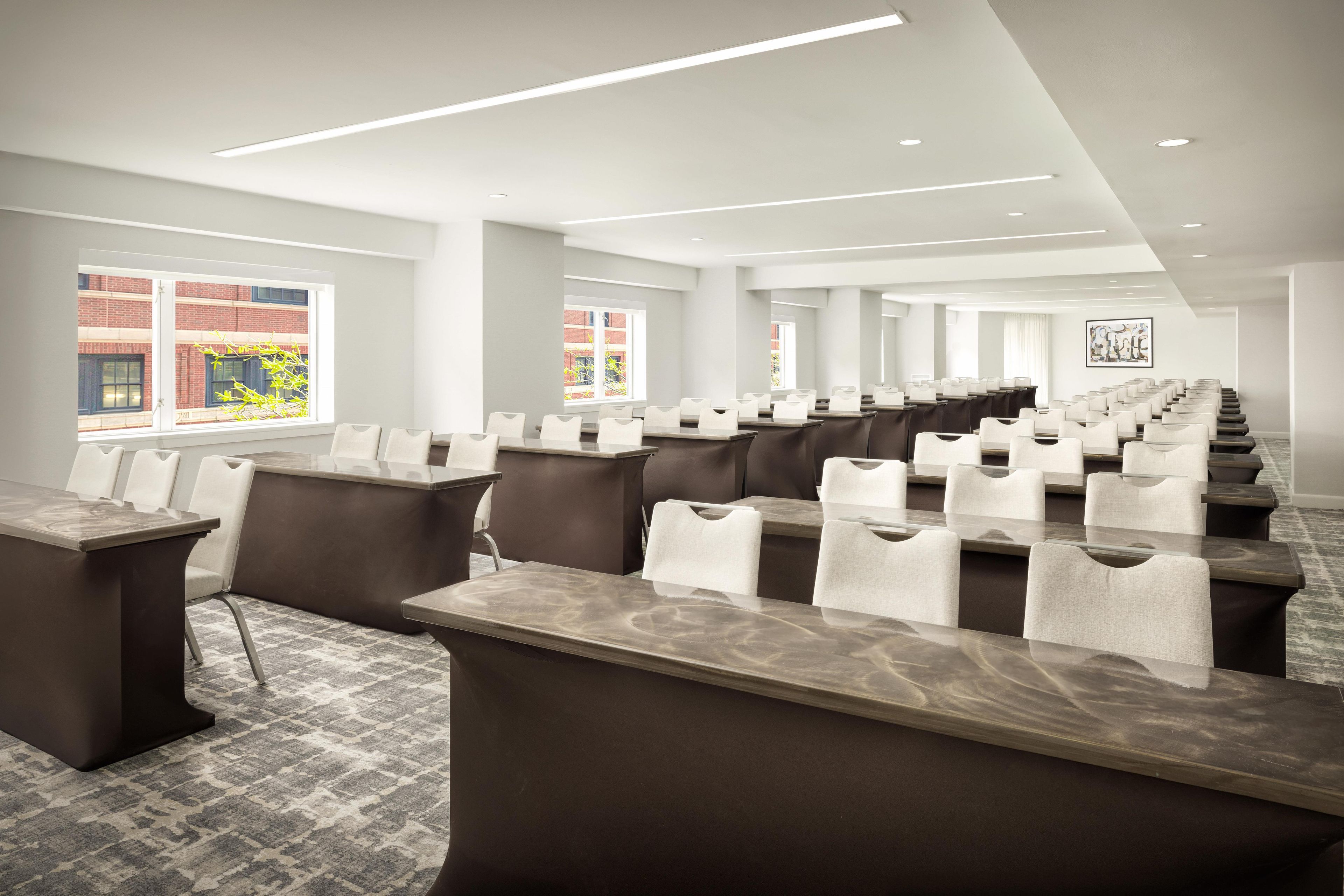 A conference room with long tables and chairs, large windows, and a modern ceiling design.