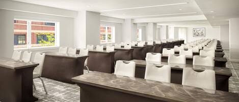 A conference room with long tables and chairs, large windows, and a modern ceiling design.