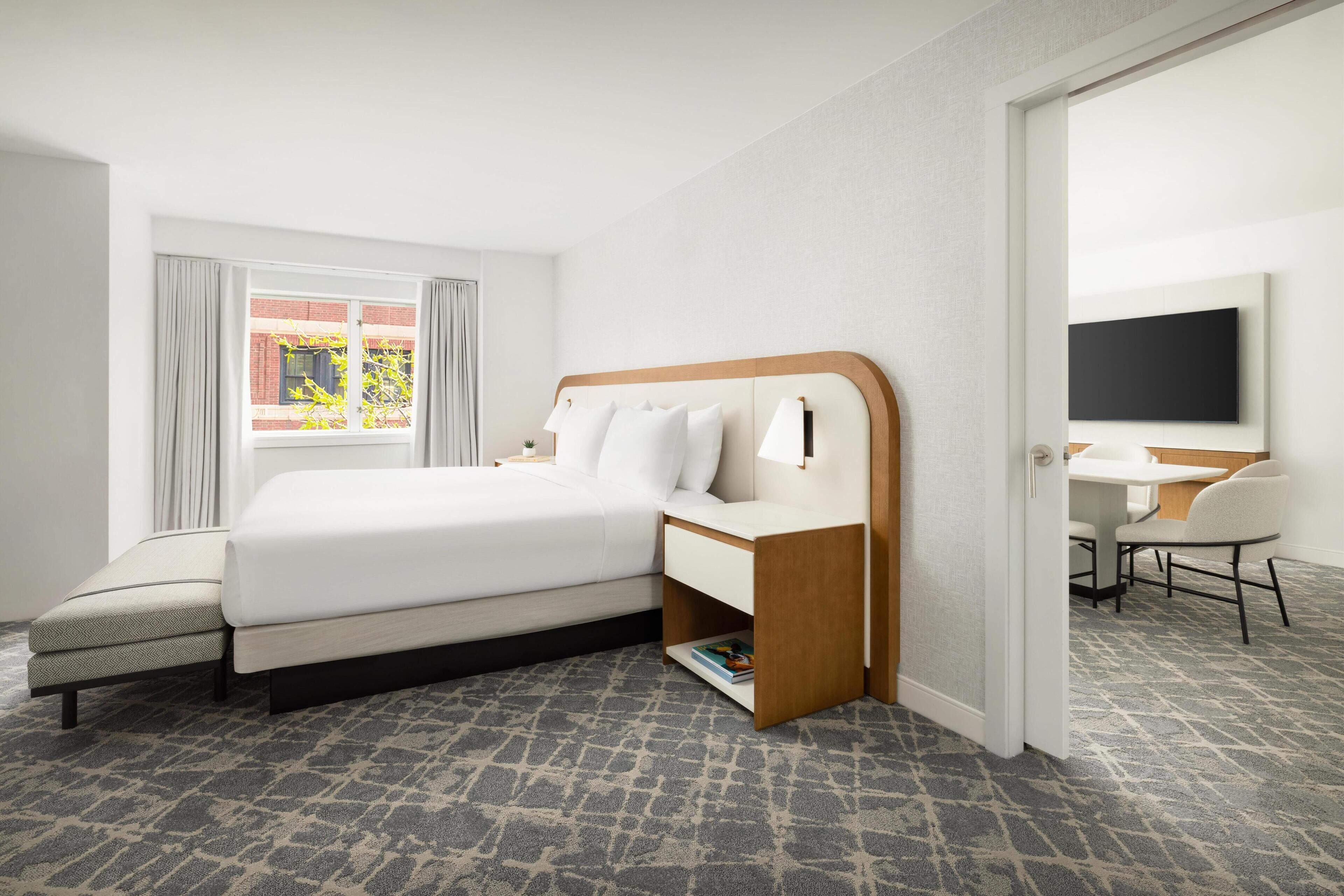 A hotel room with a bed, bedside table, lamp, chair, desk, and a TV.