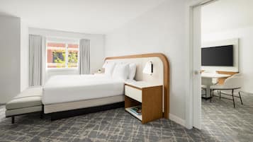 A hotel room with a bed, bedside table, lamp, chair, desk, and a TV.