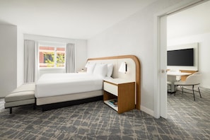 Een hotelkamer met een bed, nachtkastje, lamp, stoel, bureau en een televisie.