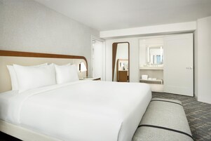A hotel room with a large bed, a bedside table, a mirror, a wardrobe, and a bathroom visible through an open door.