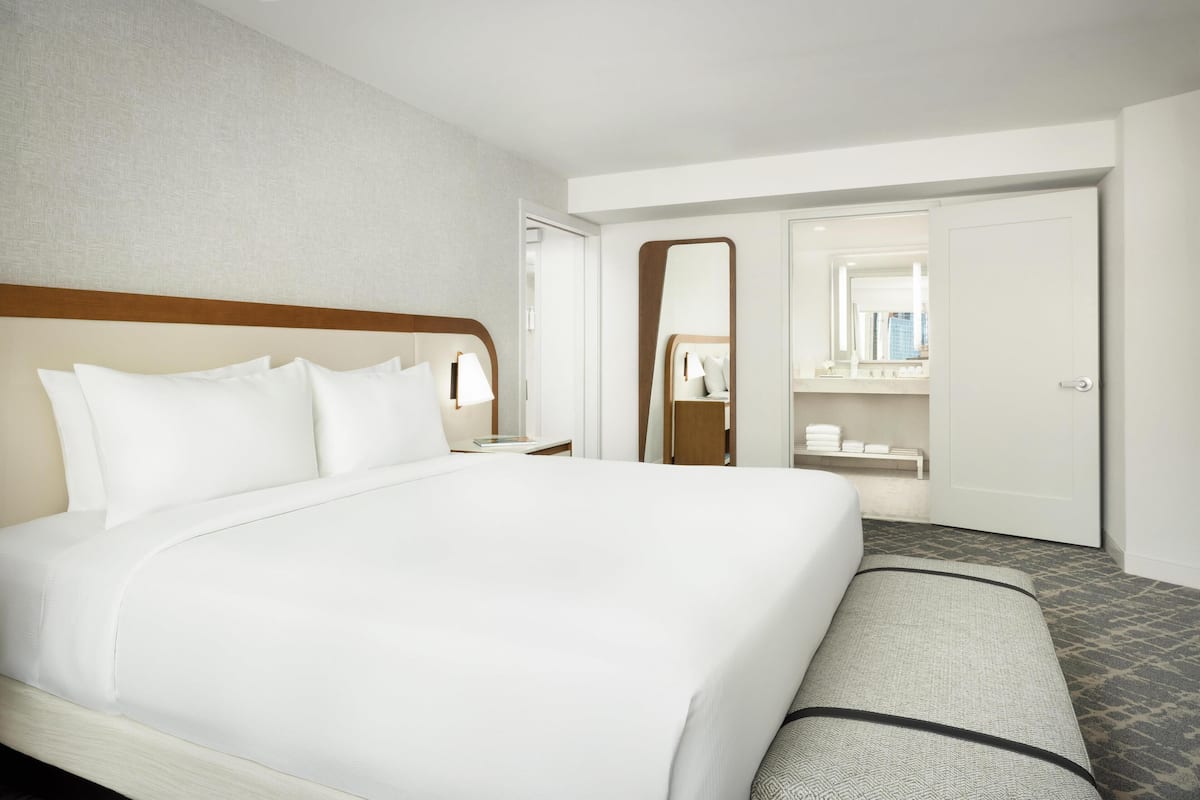 A hotel room with a large bed, a bedside table, a mirror, a wardrobe, and a bathroom visible through an open door.
