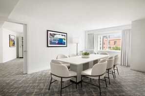 A modern hotel room with a large dining table, six chairs, a floor lamp, a framed picture, and a view of buildings through the window. - Hilton Boston Back Bay (Boston)