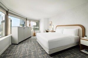 Habitación de hotel con una cama grande, un escritorio, una silla, una ventana con vista a edificios y una planta en maceta.