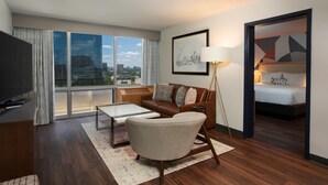Una habitación de hotel con un ventanal grande, un sofá, una mesa de centro, una lámpara y una cama.
