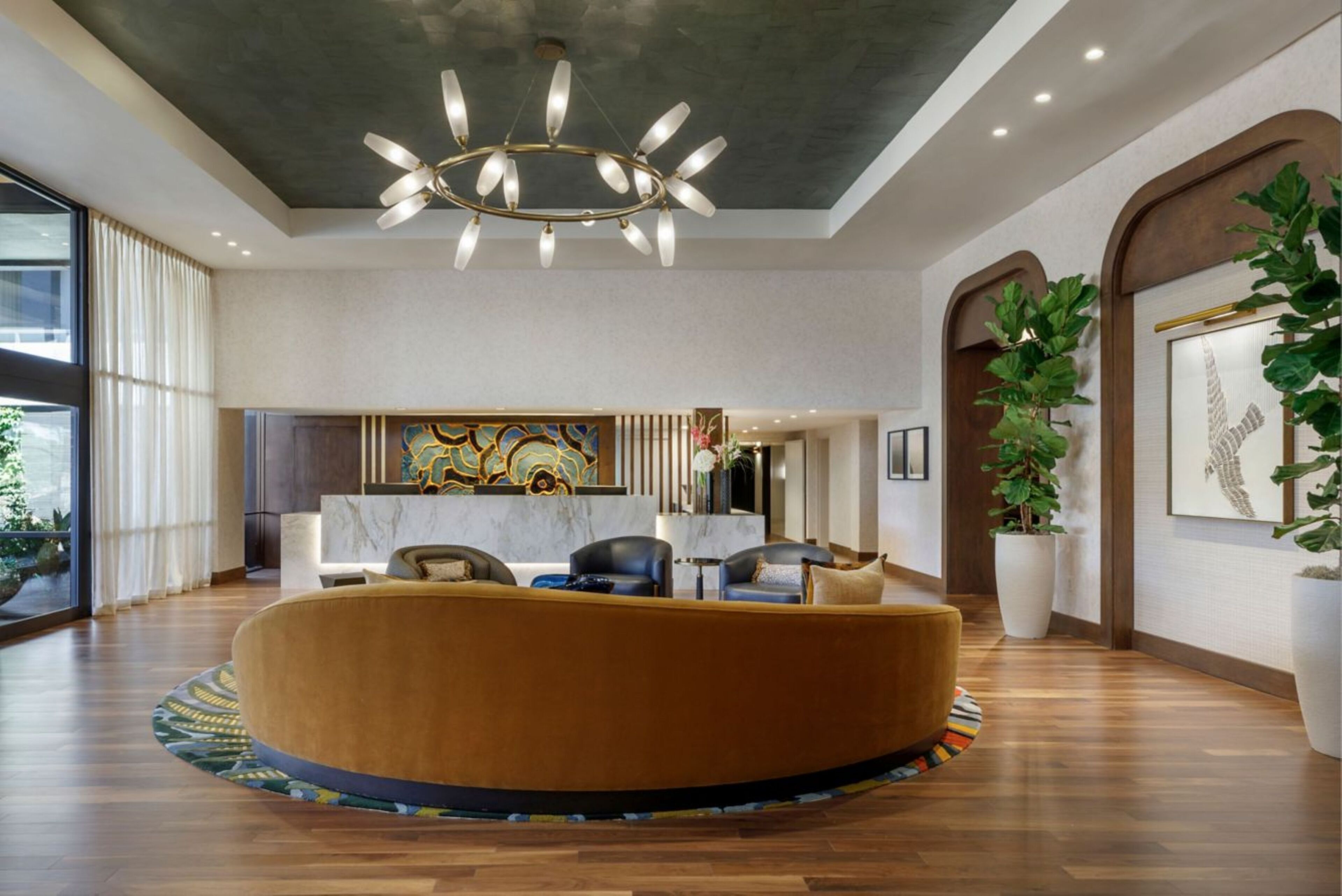 A modern lobby with a round seating area, a chandelier, and large windows.