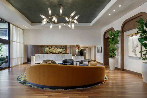A modern lobby with a round seating area, a chandelier, and large windows.